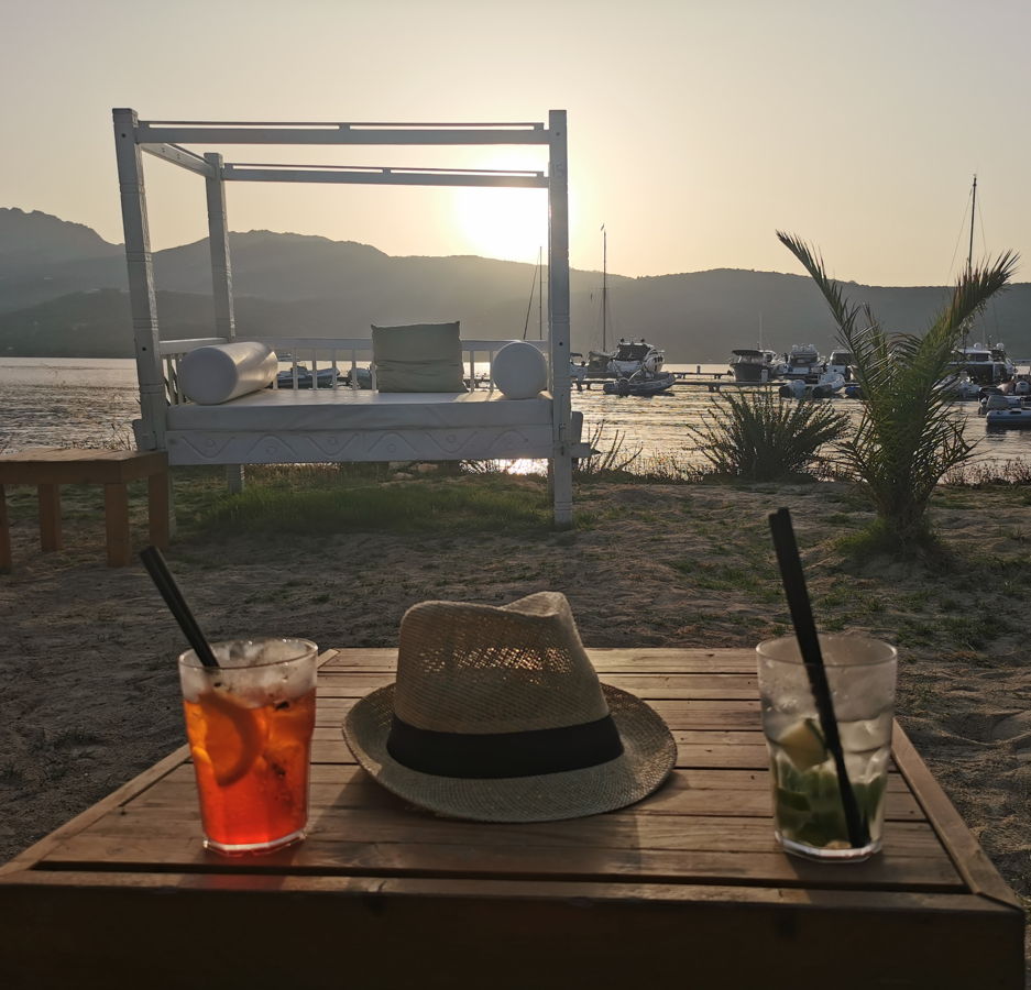 Tagesbett und ein Tisch mit Sonnenhut und zwei Cocktails in einer Beachbar auf Sardinien.