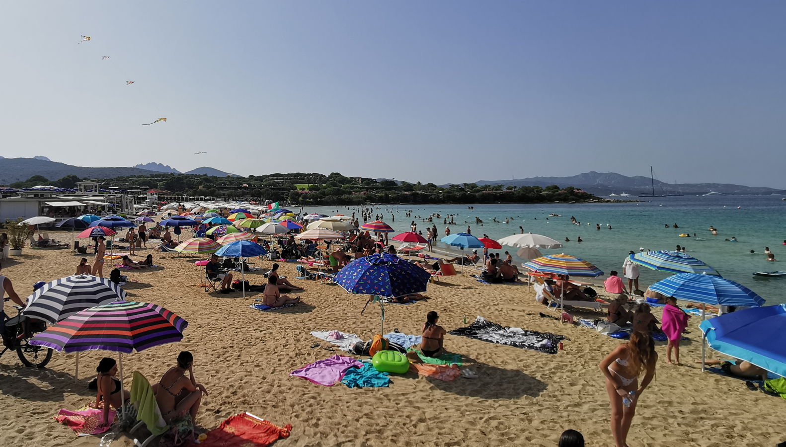 Ein Strand mit vielen bunten Sonnenschirmen und Urlaubern auf Sardinien.